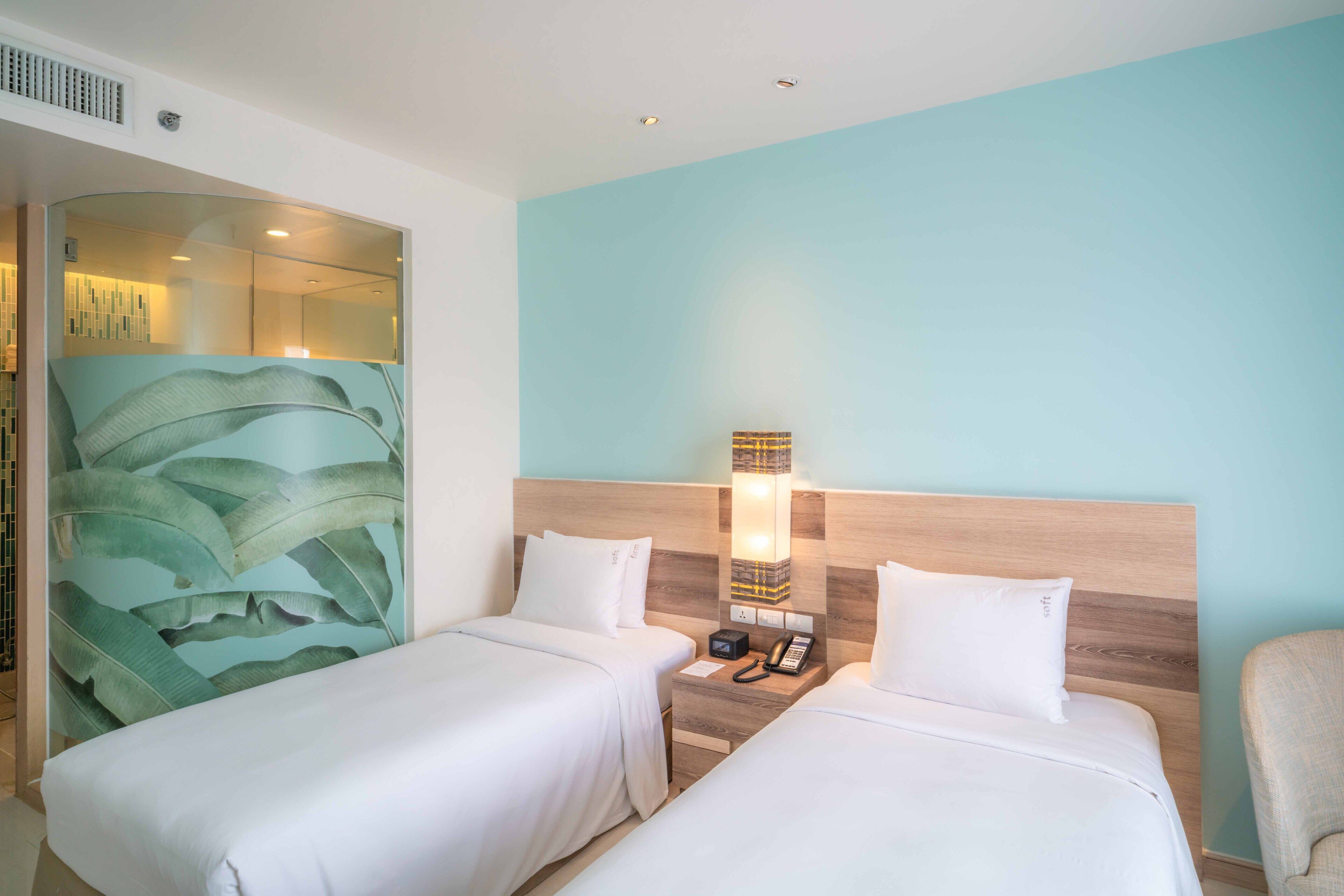 A hotel room with two single beds, a nightstand with a phone, and a wall-mounted light fixture.