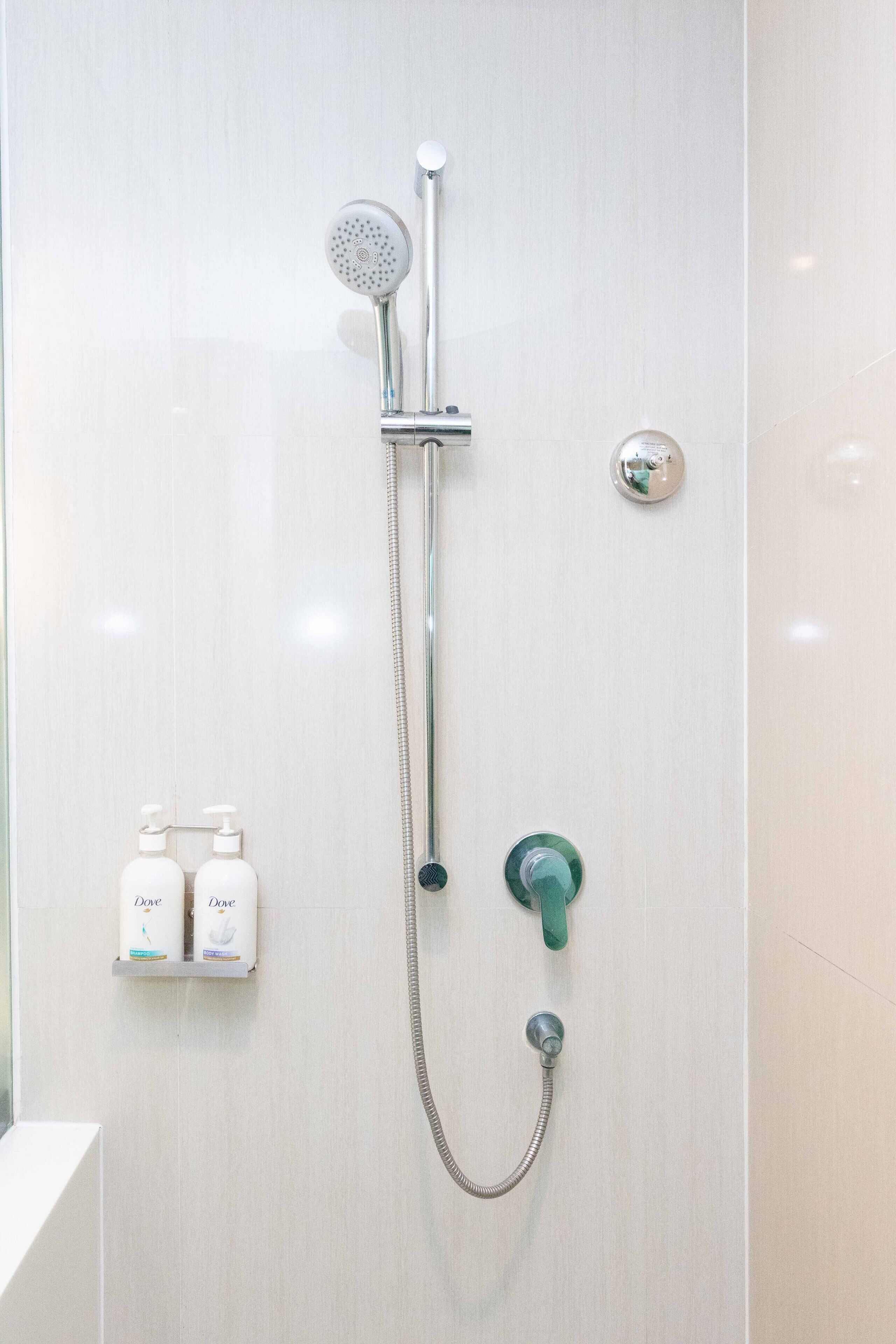 Une douche équipée d’un pommeau de douche à main, d’un robinet mural et de deux distributeurs de savon pour les mains de la marque Dove.