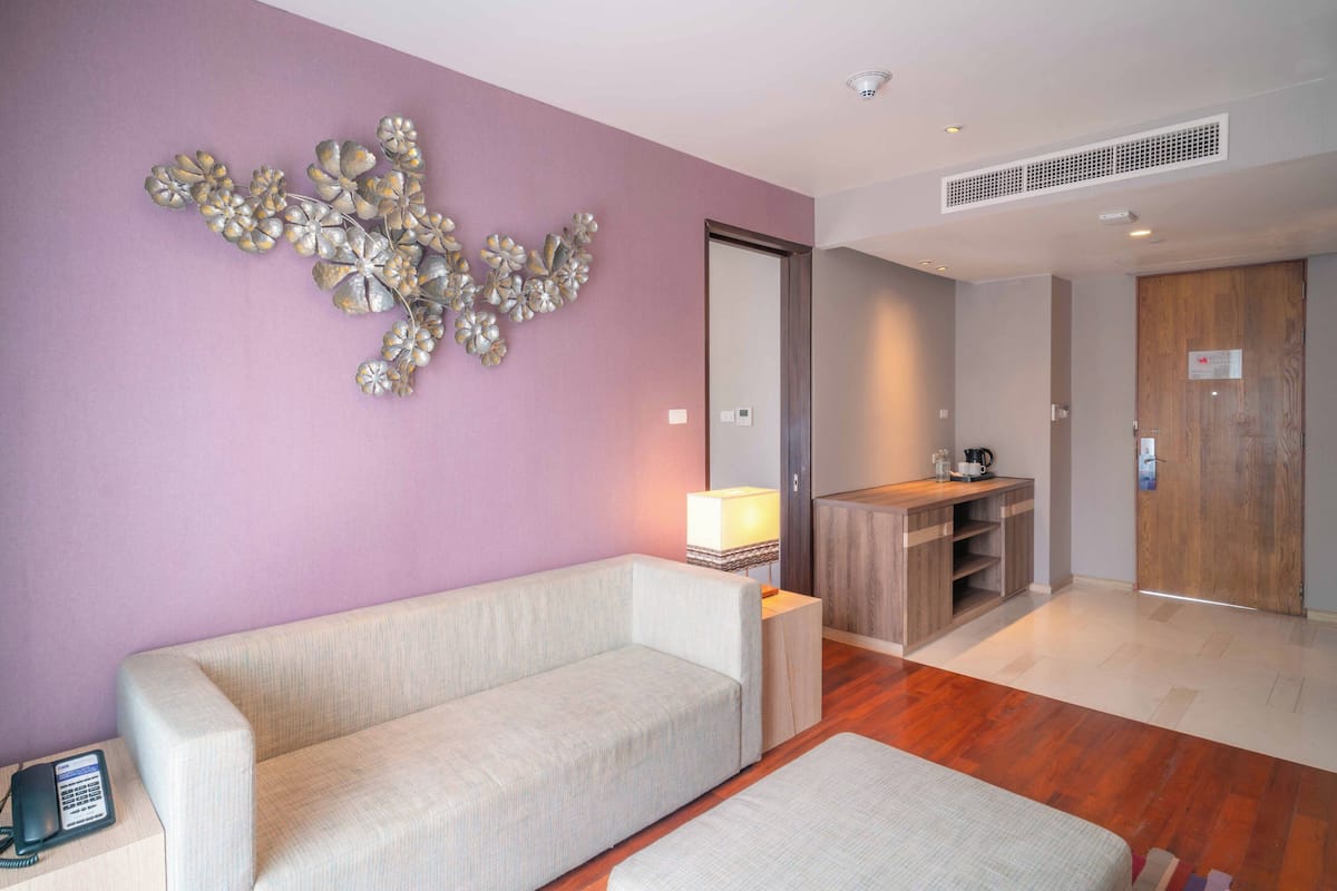 Une chambre d’hôtel moderne, équipée d’un canapé, d’une petite table, d’une lampe, d’une armoire en bois et d’un miroir.