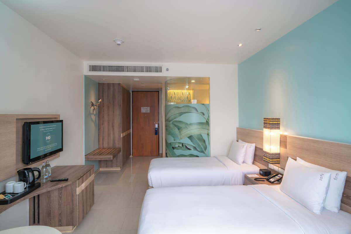 Une chambre d’hôtel avec deux lits, un bureau avec une télévision, une machine à café et une petite table avec des tasses et une télécommande.