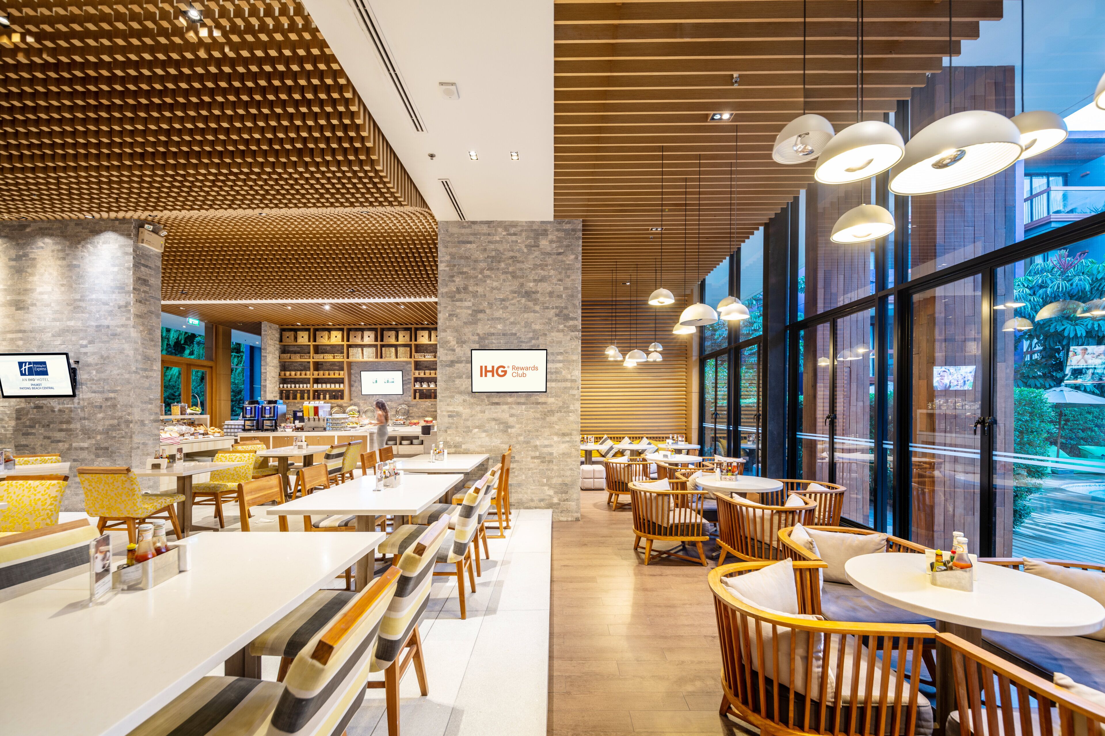 A modern hotel lobby with a central seating area, a coffee bar, and a view of the outdoors.