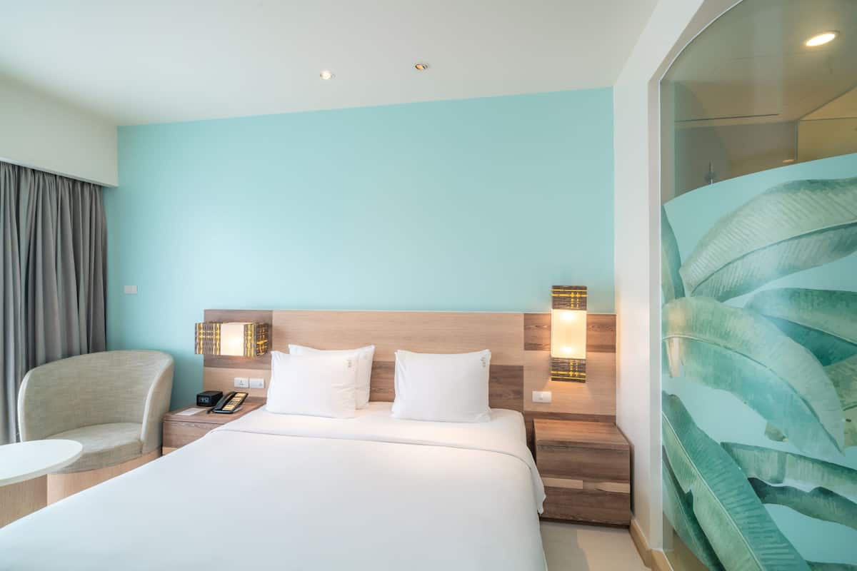 Une chambre d’hôtel comprenant un lit, une chaise, une table de chevet, un téléphone et un mur orné d’un motif de feuilles.