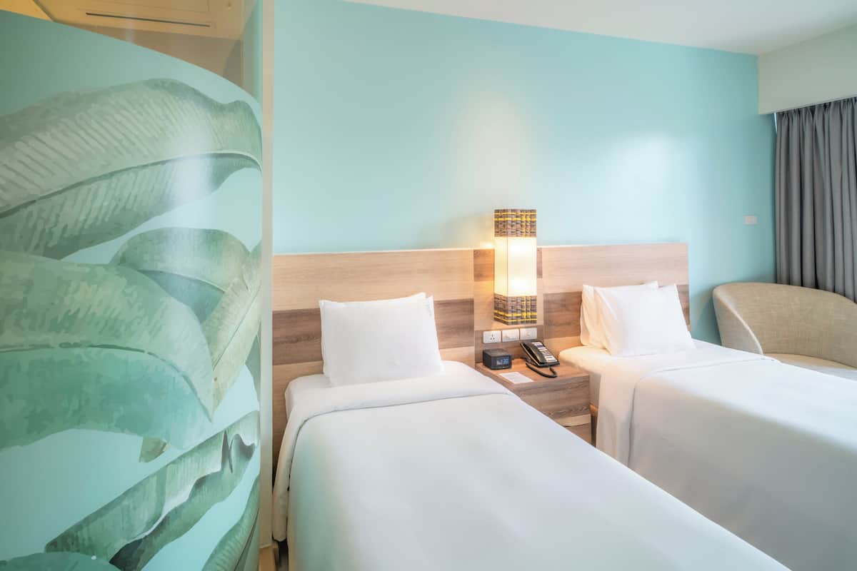 Une chambre d’hôtel avec deux lits, une table de chevet avec une lampe et une grande plante.