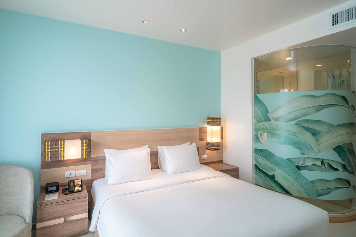 Une chambre d’hôtel comprenant un lit, des tables de chevet, une chaise et un grand miroir orné d’un motif de feuilles.