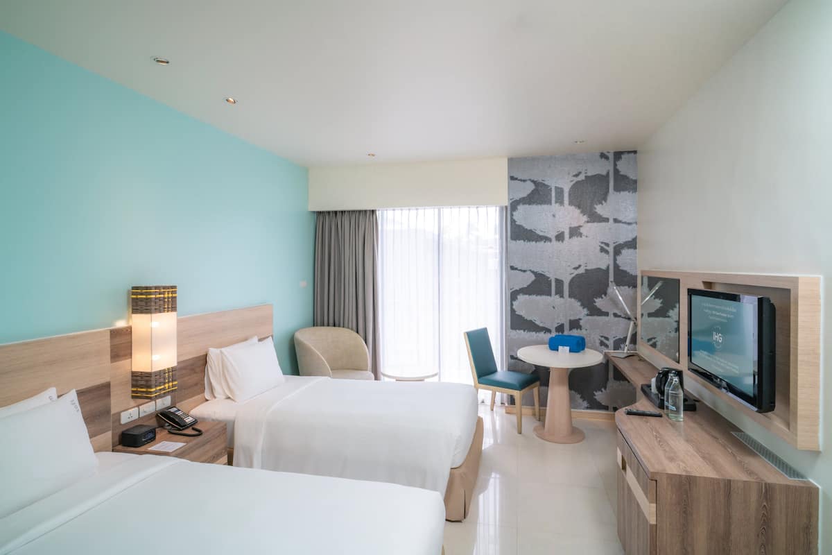 Une chambre d’hôtel avec deux lits, un bureau avec une télévision, une petite table et une chaise.