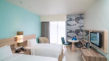A hotel room with two beds, a desk with a TV, a small table, and a chair.