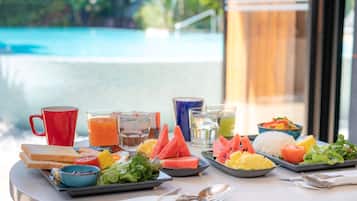 A breakfast buffet with various food items, drinks, and a red mug on a table with a pool view.