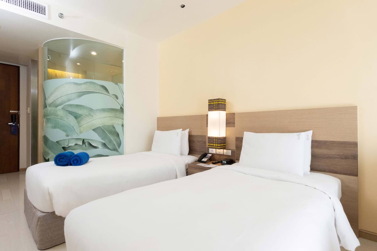 Une chambre d’hôtel avec deux lits, une cloison en verre, une table de chevet avec un téléphone et un luminaire fixé au mur.