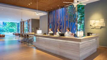 Zona de recepción de un hotel con diseño moderno, que incluye un mostrador de recepción, taburetes de bar y vistas al exterior.
