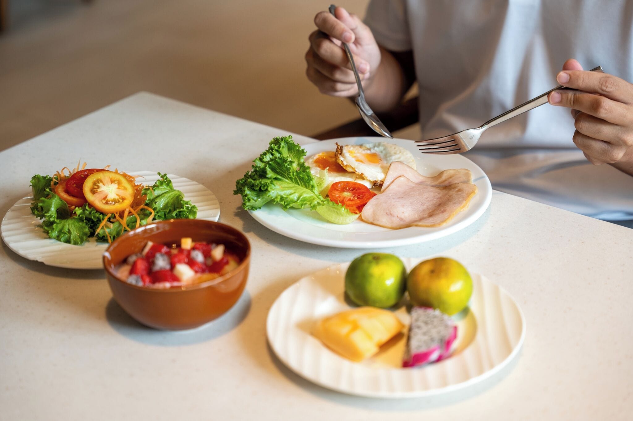 Una mesa de comedor con platos de comida, un tazón de ensalada de frutas y un plato con dos limones.