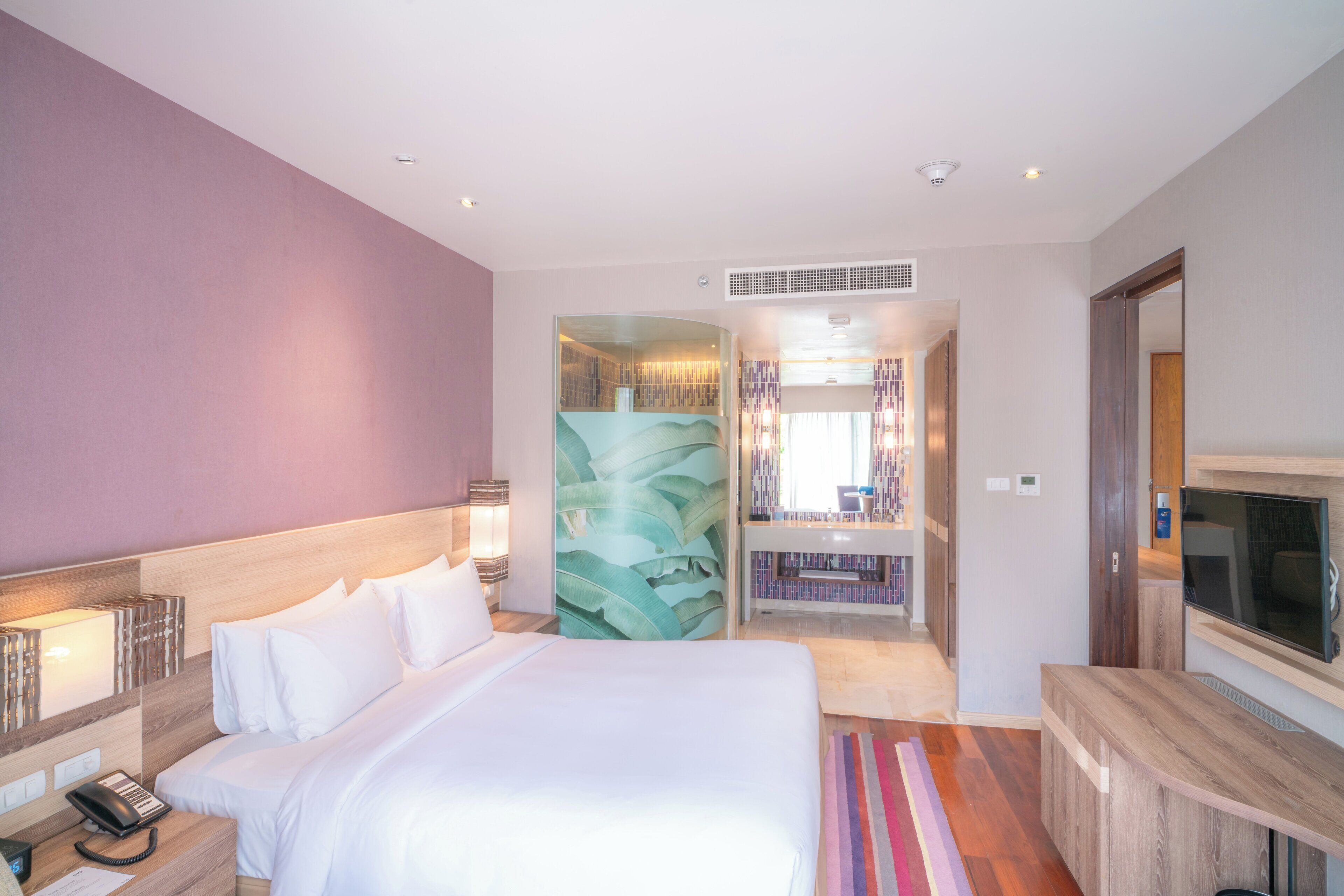 A hotel room with a bed, bedside table, phone, and a TV.