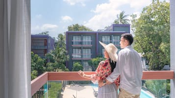 Un balcón con vistas a un edificio moderno, palmeras y una zona de piscina.