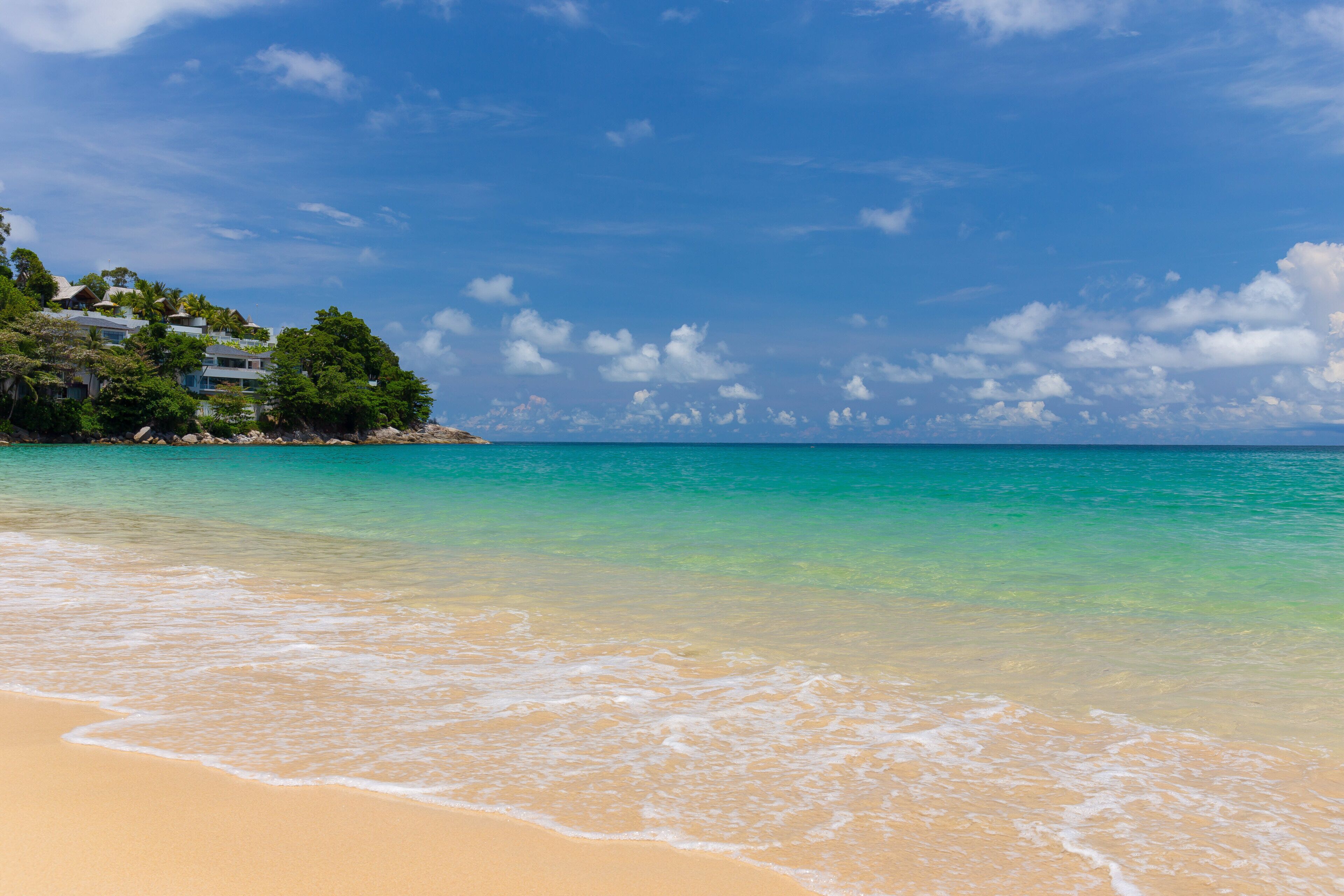A beach with clear turquoise water, sandy shore, and a building with a view of the ocean.