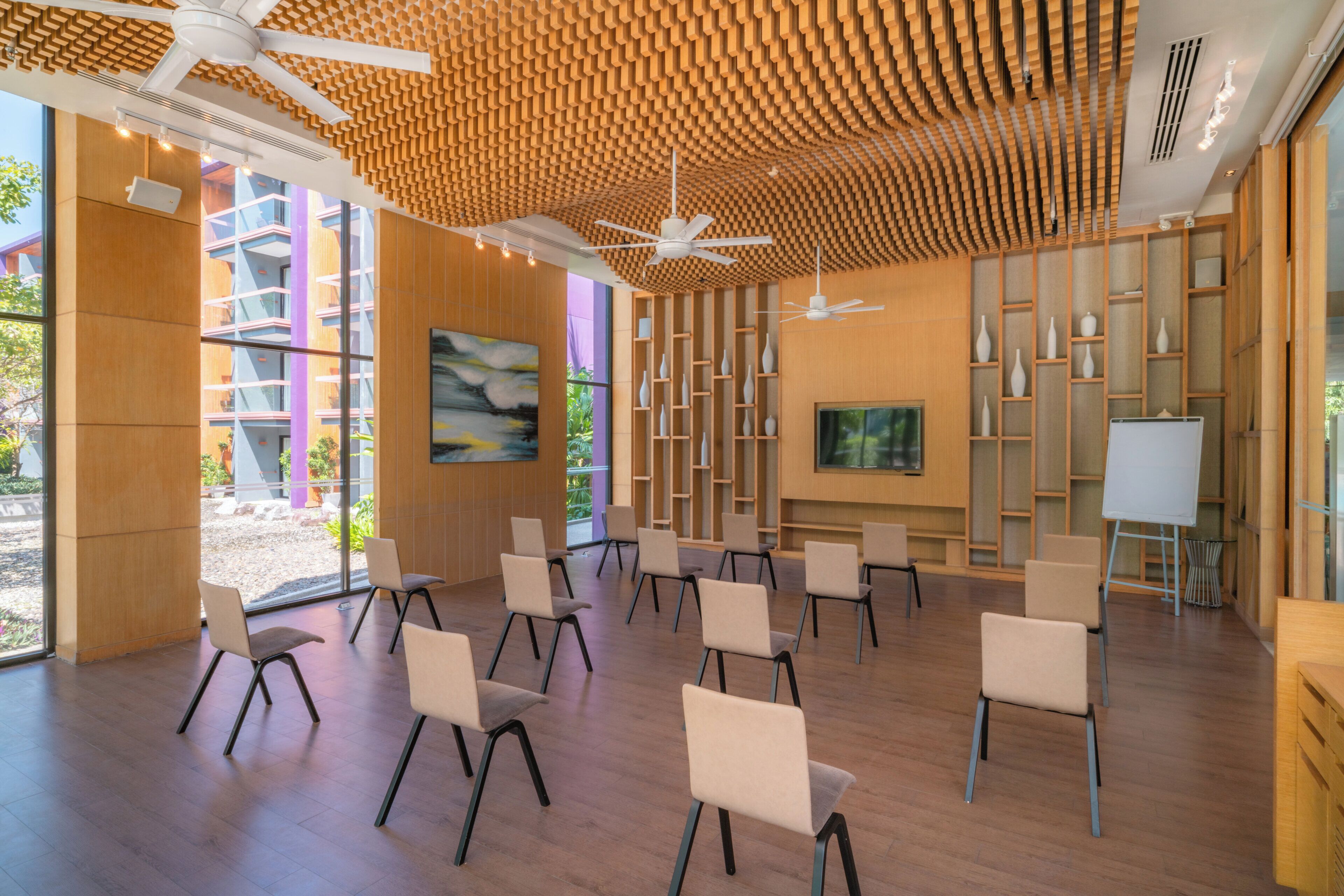 Een congreszaal met een modern design, met een houten plafond, een groot schilderij en een whiteboard.