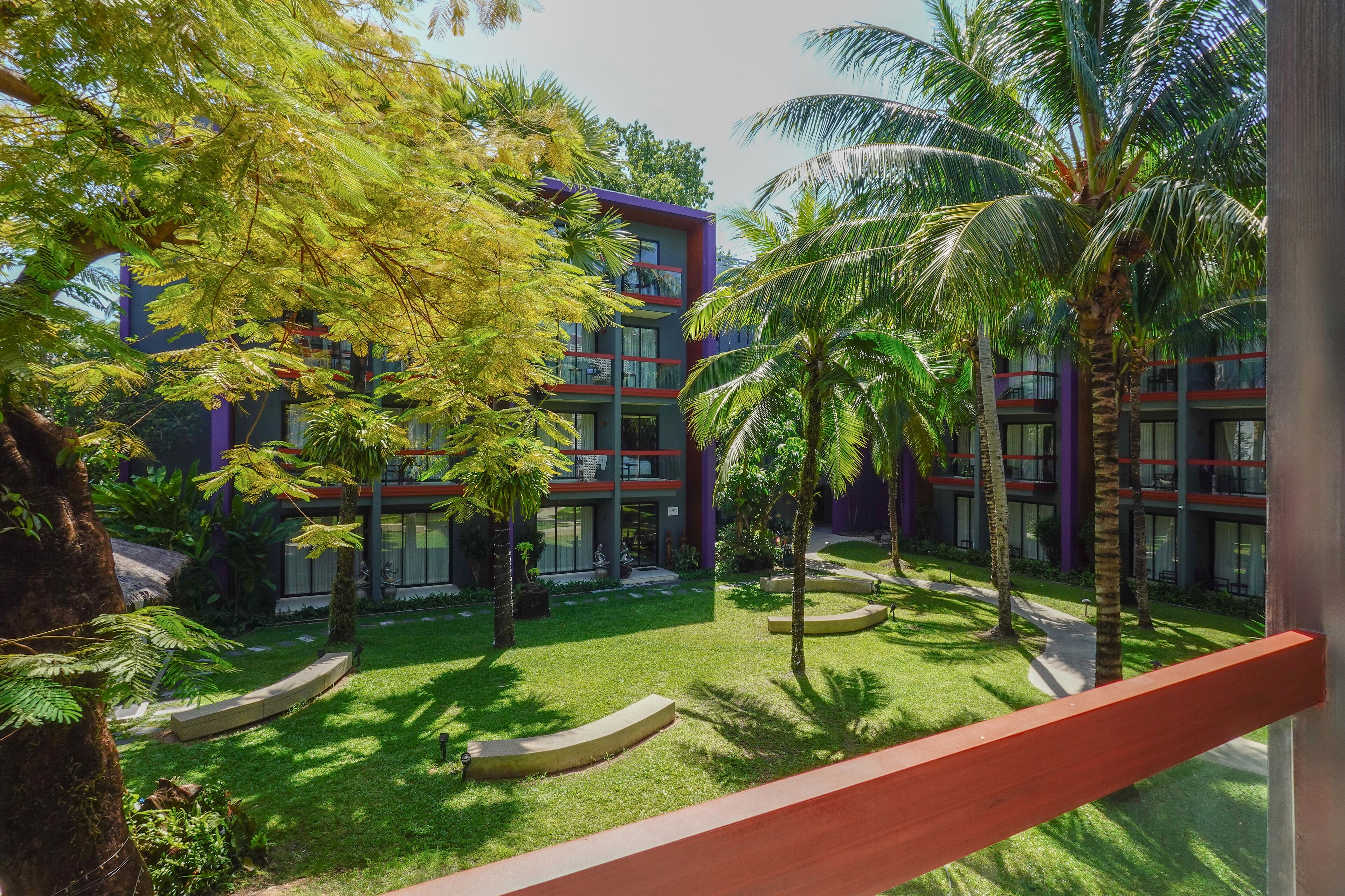 Un bâtiment moderne doté de nombreux balcons, entouré d’une végétation luxuriante et de palmiers.