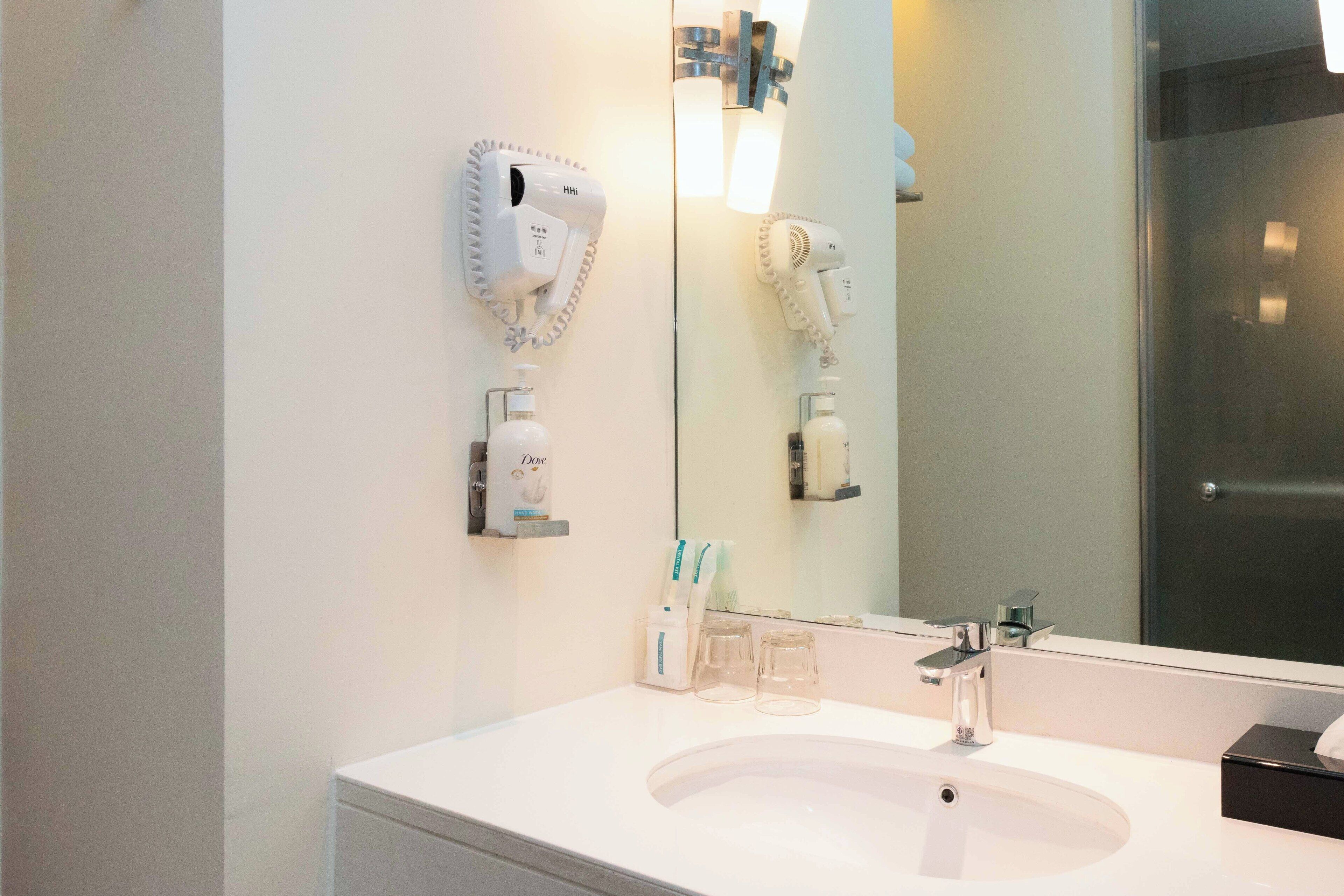 A modern bathroom with a white sink, a large mirror, and two hair dryers mounted on the wall.