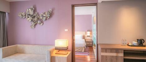 A hotel room with a sofa, a bedside table with a lamp, a wooden cabinet, and a decorative wall piece.