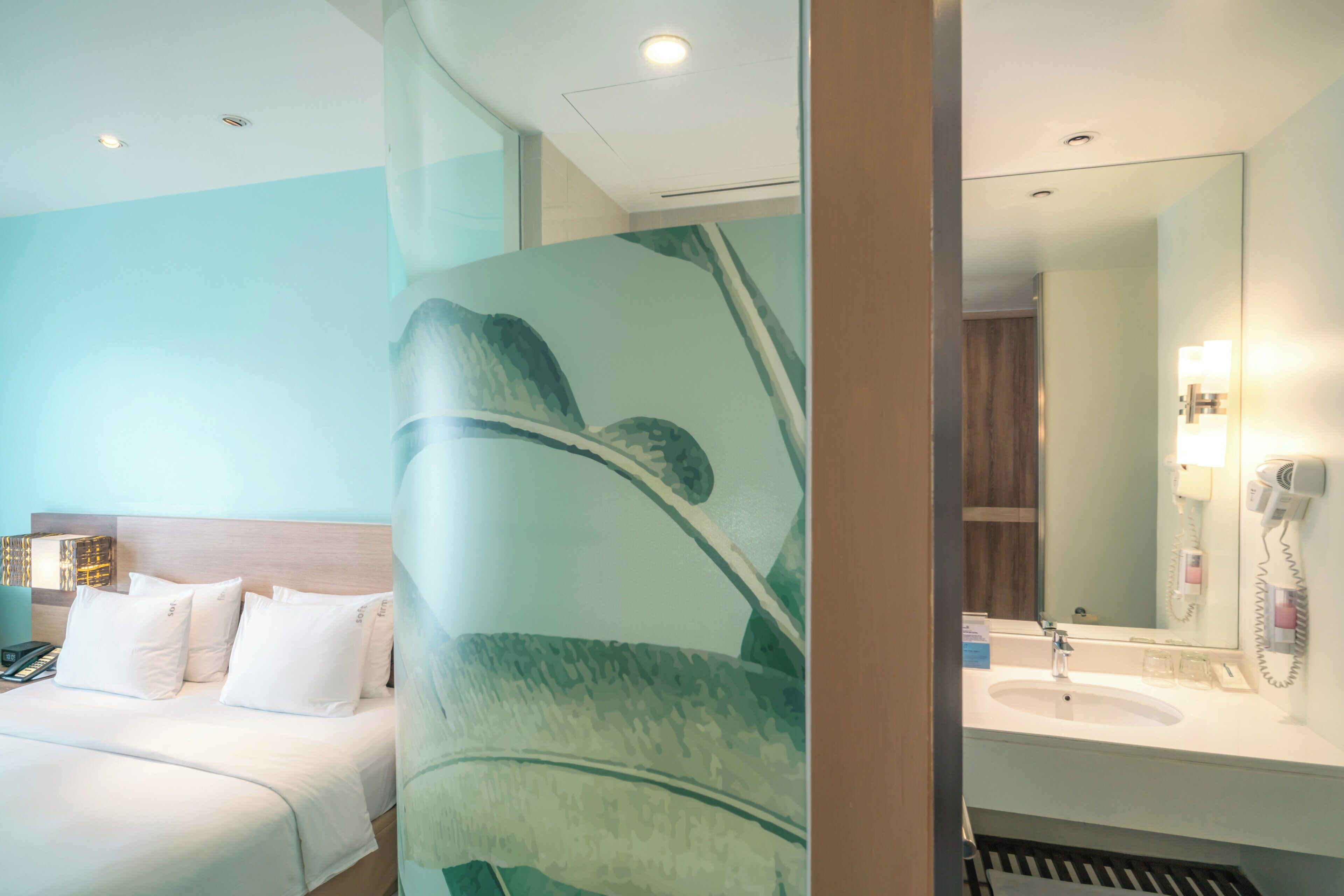 Quarto de hotel com cama, espelho grande, pia e secador de cabelo.