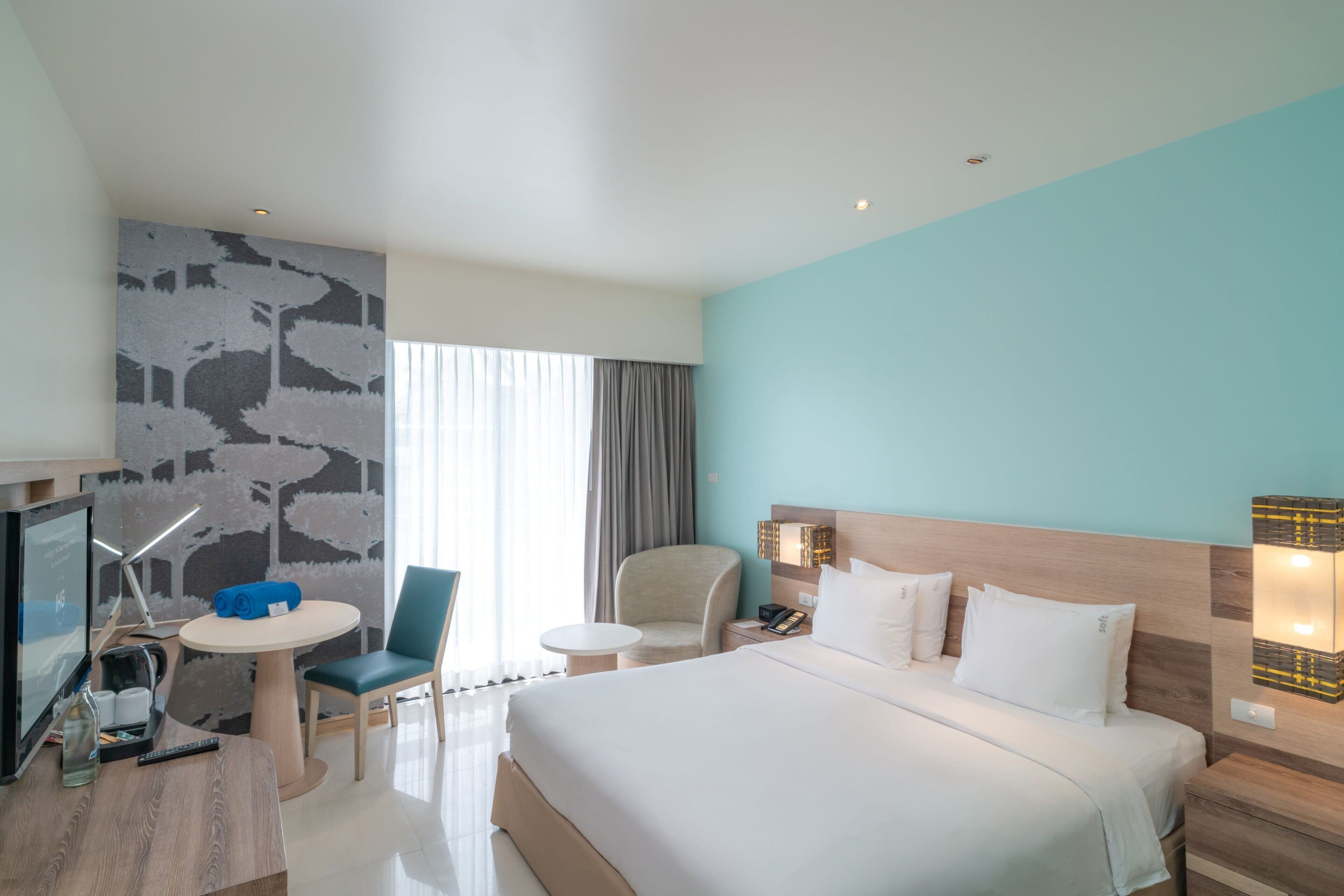 Een hotelkamer met een bed, een bureau, een stoel, een televisie en een raam met gordijnen.