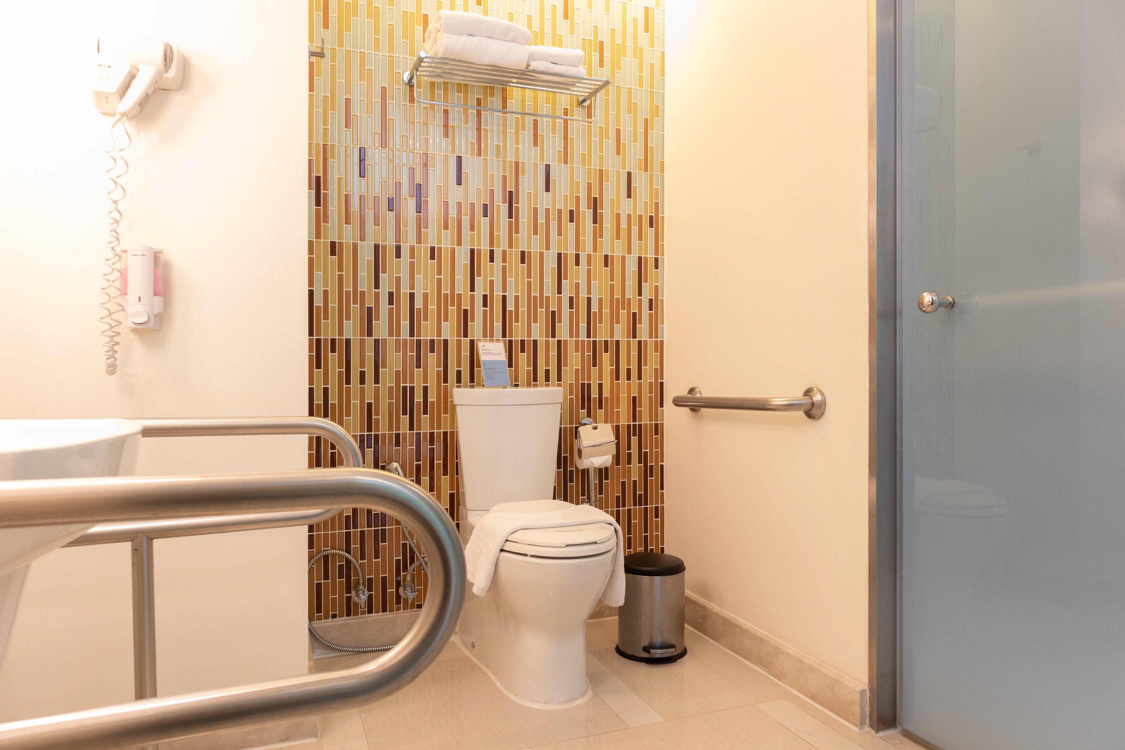 Un baño con inodoro, secamanos, cubo de basura y un perchero para toallas.