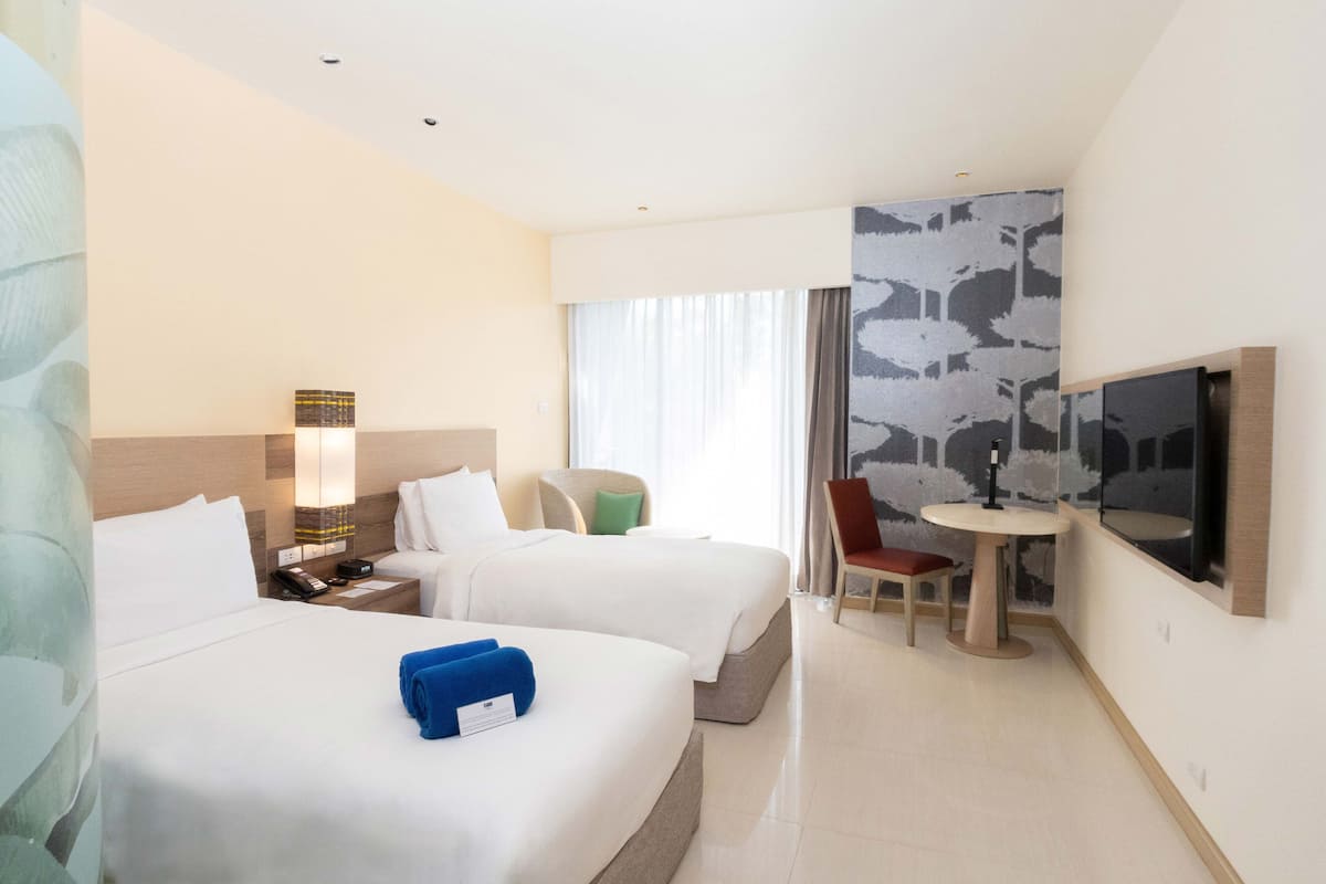 Une chambre d’hôtel avec deux lits, un bureau avec une chaise, une télévision et une grande fenêtre avec des rideaux.