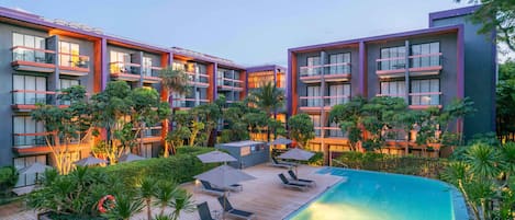 Un hotel moderno con zona de piscina, varios balcones y abundante vegetación.