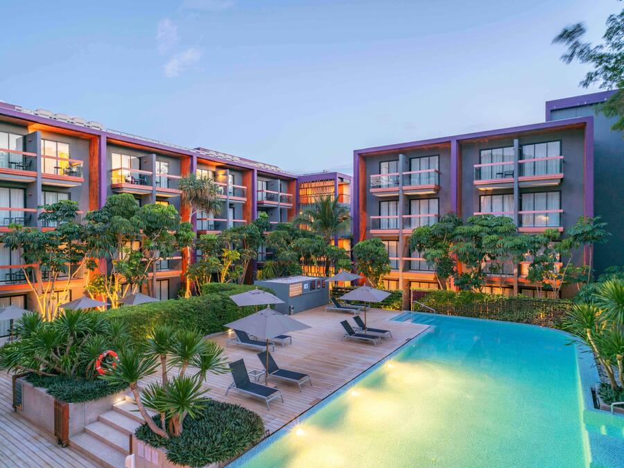 Un hotel moderno con zona de piscina, varios balcones y abundante vegetación.