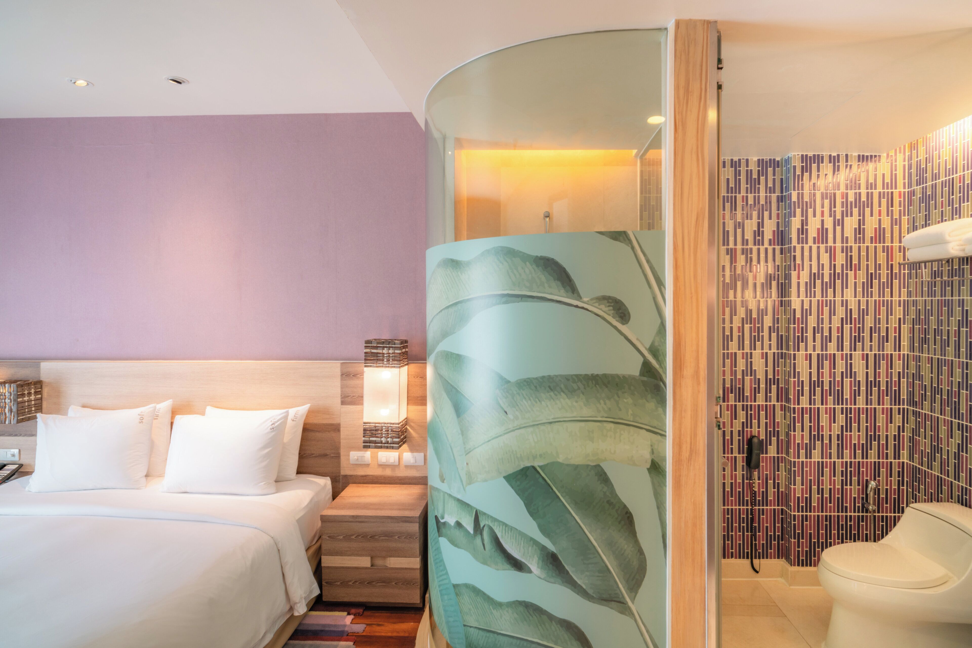 A hotel room with a bed, a nightstand, a lamp, a shower area, and a bathroom.