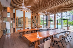 A modern conference room with wooden tables and chairs, large windows, and ceiling fans.