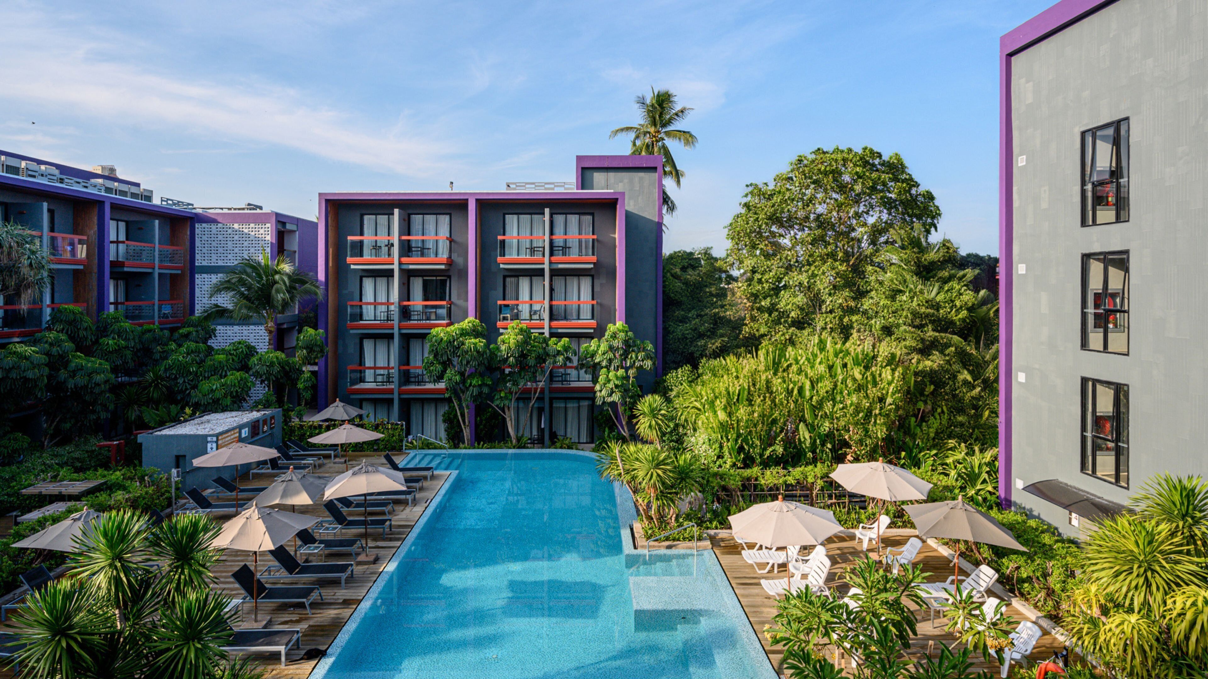 A hotel with a swimming pool, multiple balconies, and lush greenery.
