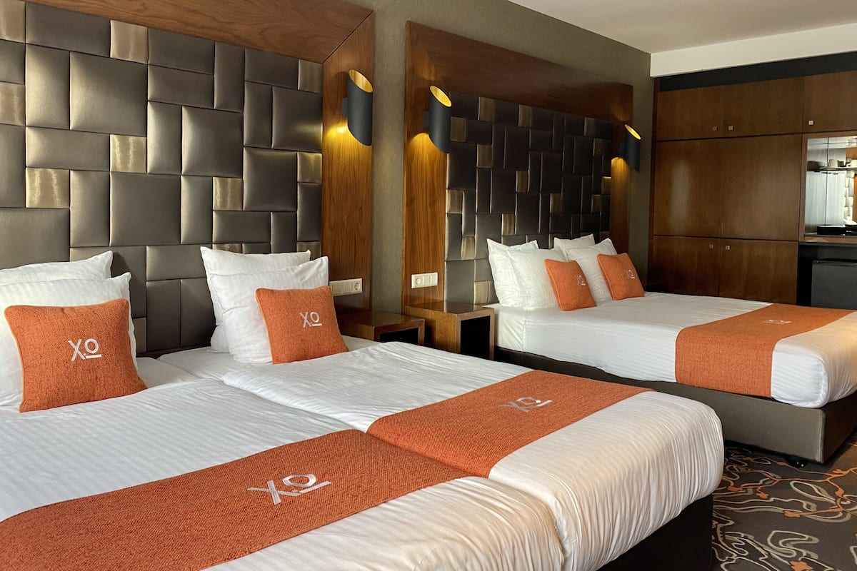 Une chambre d’hôtel avec deux lits, une tête de lit en bois, un minibar et un petit coin cuisine.