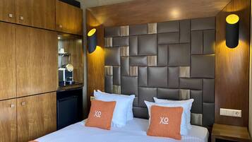A hotel room with a large bed, wooden wardrobe, and a modern headboard with built-in lighting.