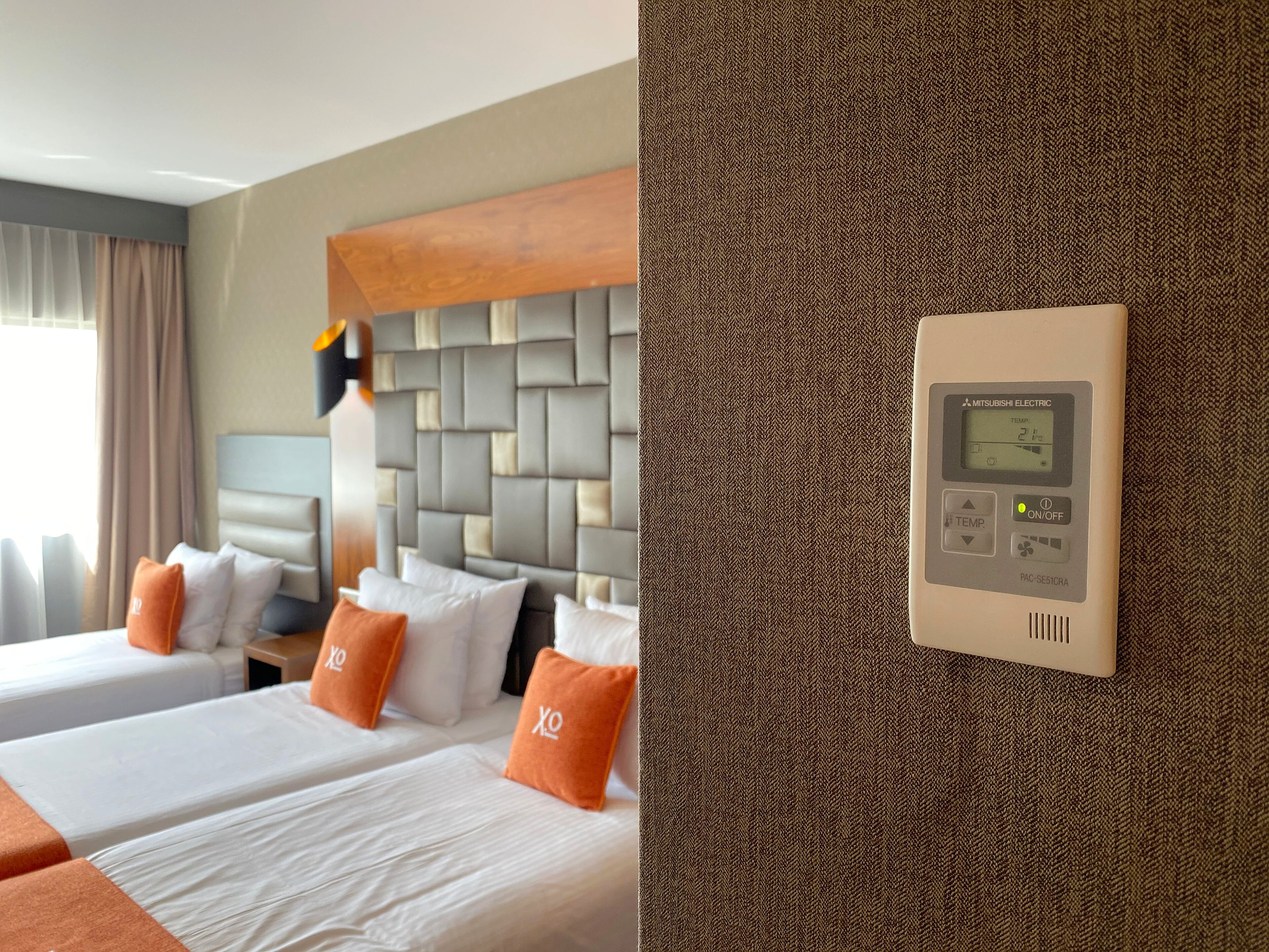 A hotel room with two beds, a modern headboard, and a wall-mounted thermostat.