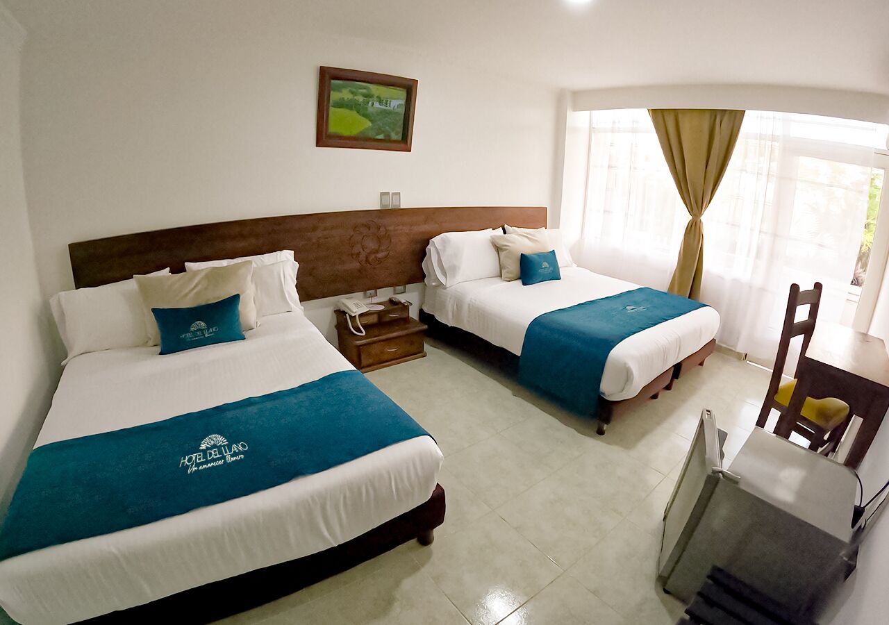 A hotel room with two beds, a desk, and a chair. There is a painting on the wall and a window with curtains.