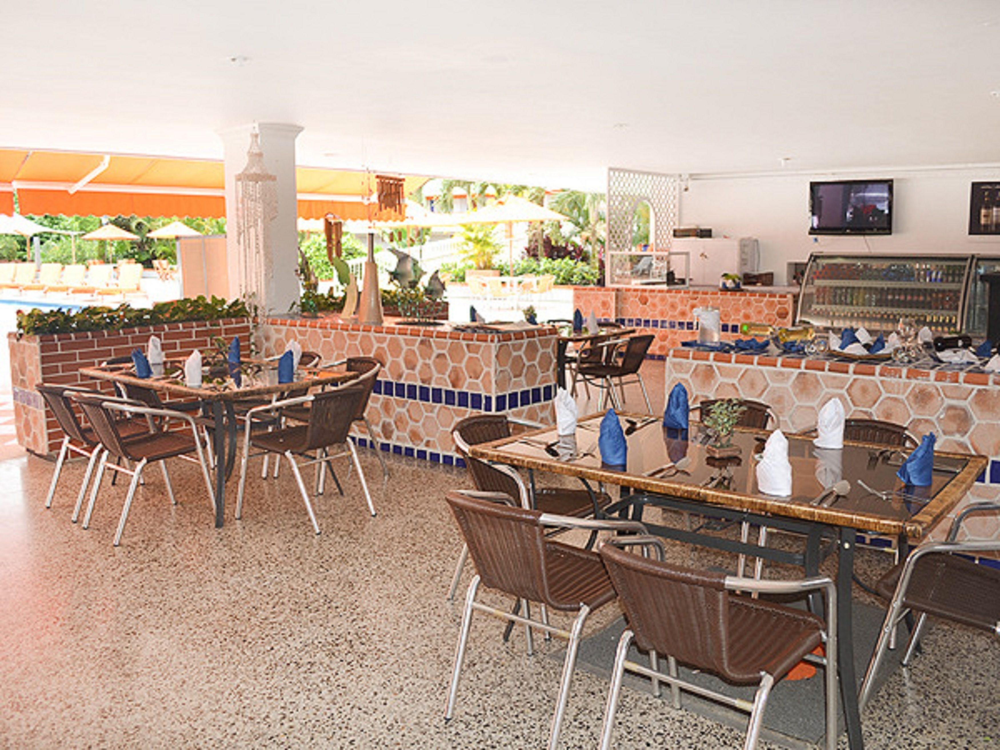 An outdoor dining area with tables and chairs, a pool, and a bar area with a tiled backsplash.