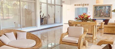Amplia sala de estar con mobiliario de mimbre, una mesa de centro de vidrio y un ventanal con vistas al exterior.