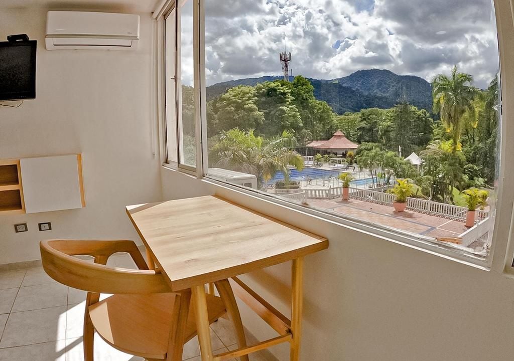 Ein Zimmer mit einem Holztisch und Stuhl, ein Fenster mit Blick auf einen Pool und Berge.