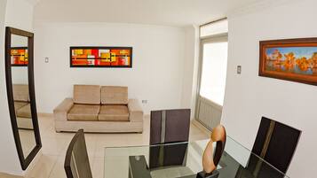 Un salón moderno con una mesa de centro de vidrio, un sofá color beige y arte abstracto en las paredes.
