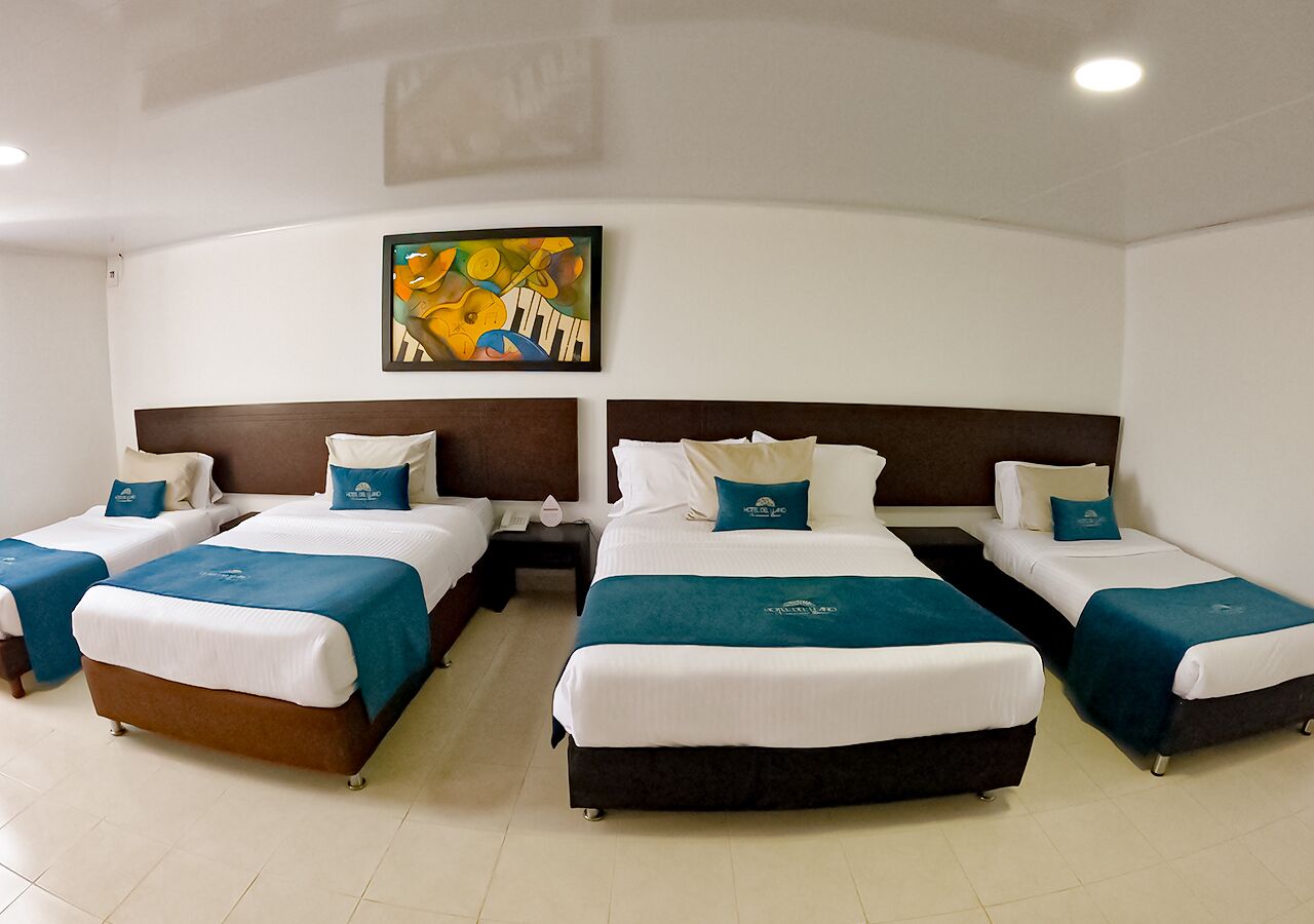 A hotel room with four single beds, a large bed, and a nightstand with a lamp.