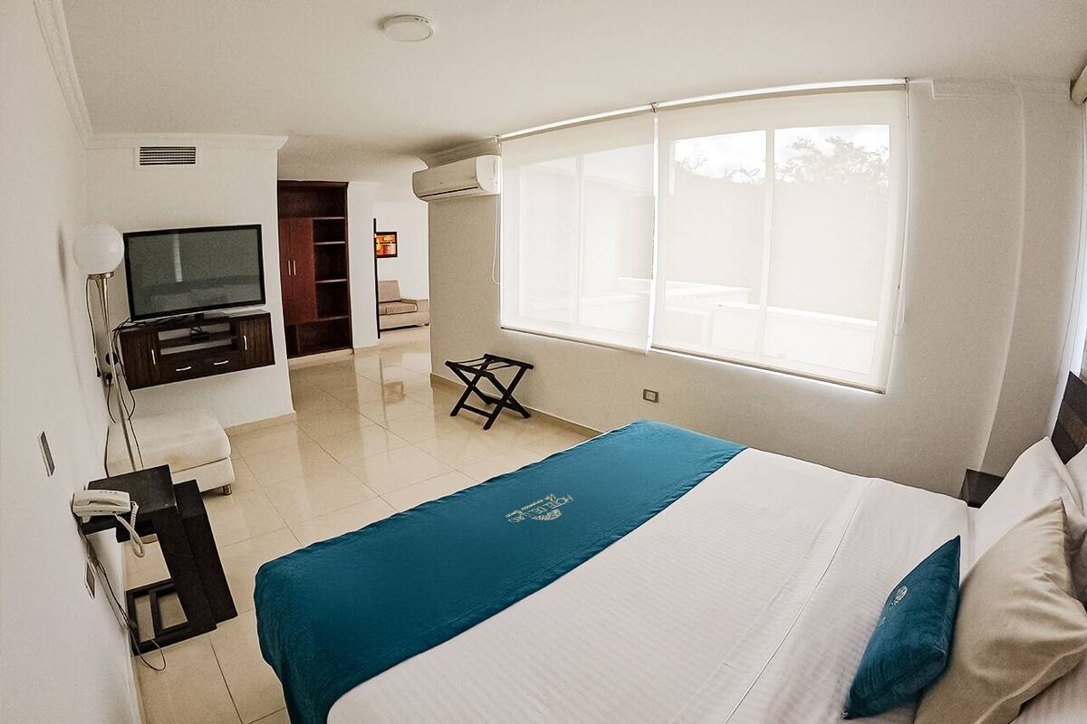 Une chambre d’hôtel avec un lit, un bureau, une chaise, une télévision et une fenêtre.