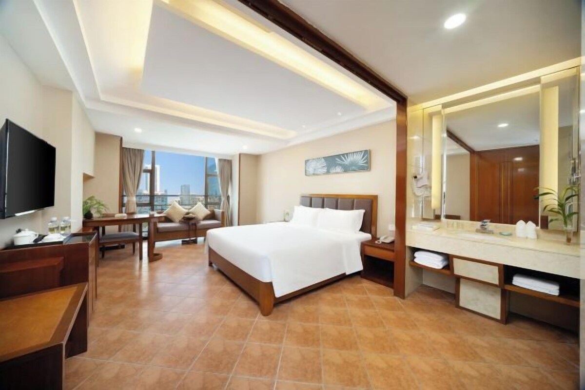 Habitación de hotel con una cama grande, un escritorio, una silla, un televisor, baño con espejo y vistas a la ciudad.