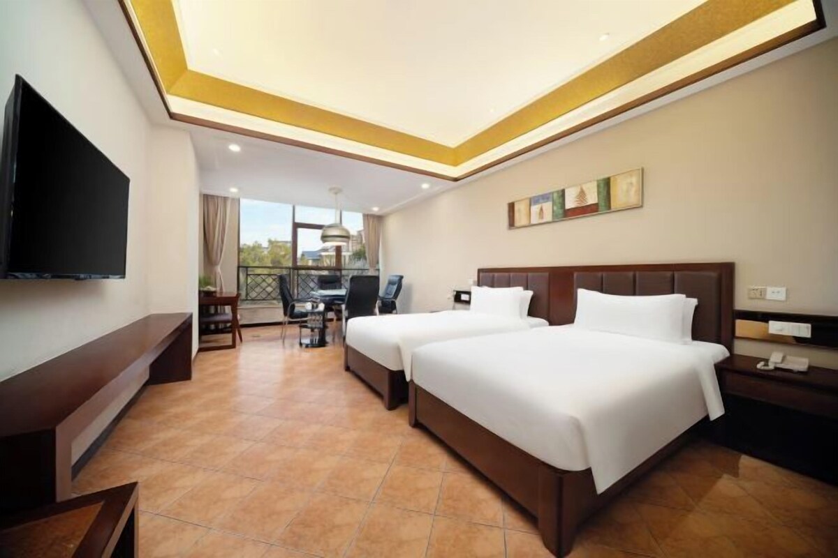 Habitación de hotel con dos camas, televisión, escritorio y balcón con vistas.
