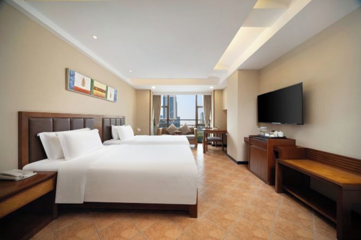 Habitación de hotel con dos camas, televisión, escritorio y vista a la ciudad.