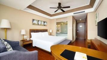 A hotel room with a bed, a desk, a chair, a sofa, a ceiling fan, and a TV.