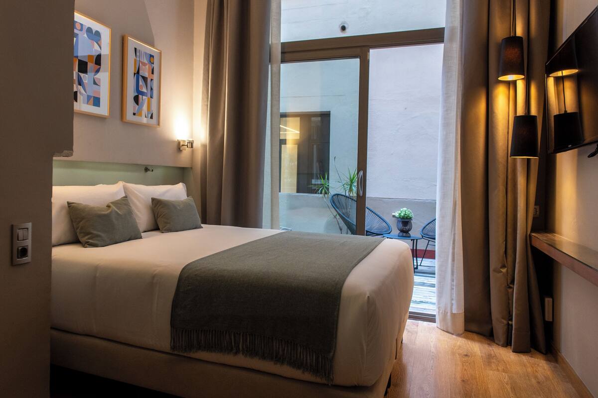 A modern hotel room with a large bed, a view to the outside, and a small balcony area.