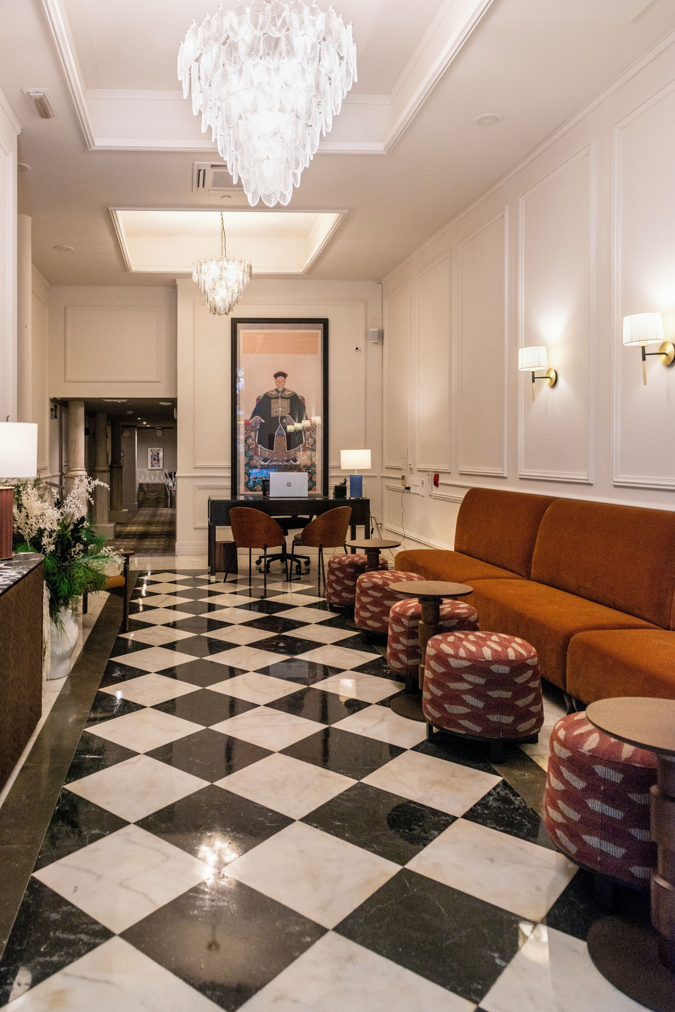 A lobby with a checkered floor, a chandelier, a sofa, and a table with chairs.