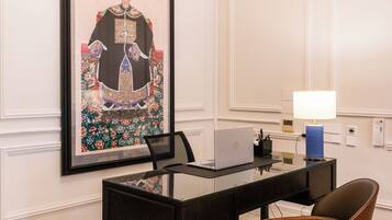 Habitación de hotel con una mesa de comedor, sillas, una computadora portátil, una obra de arte enmarcada y una lámpara.