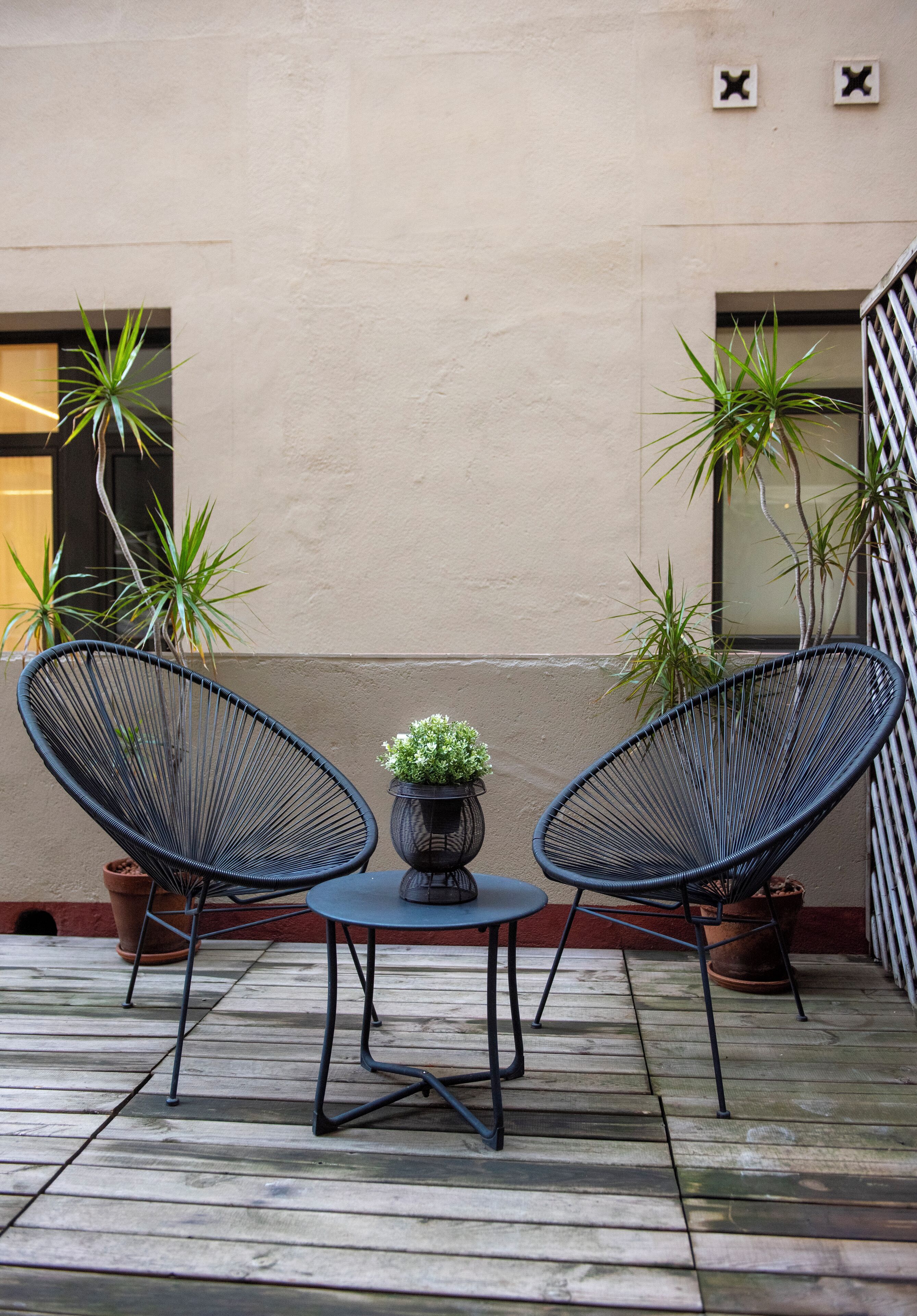 Two black wireframe chairs, a small round table, and two potted plants on a wooden deck.