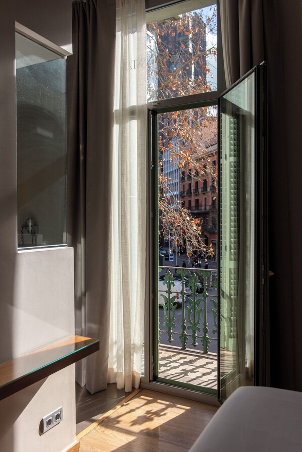 A hotel room with a large window, a bed, a bedside table, and a view of the cityscape.