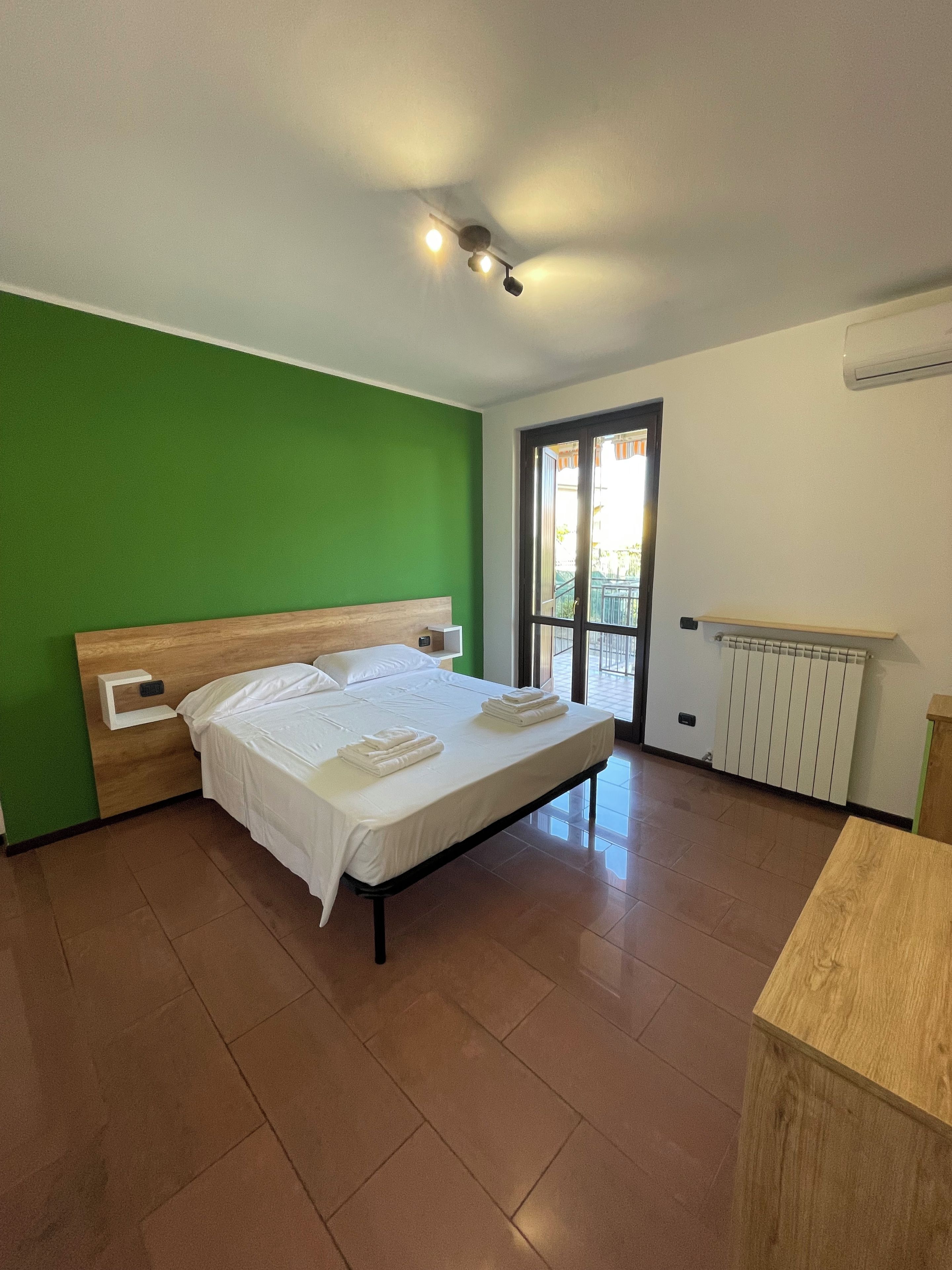 A bedroom with a bed, bedside tables, a radiator, and a view through a glass door.